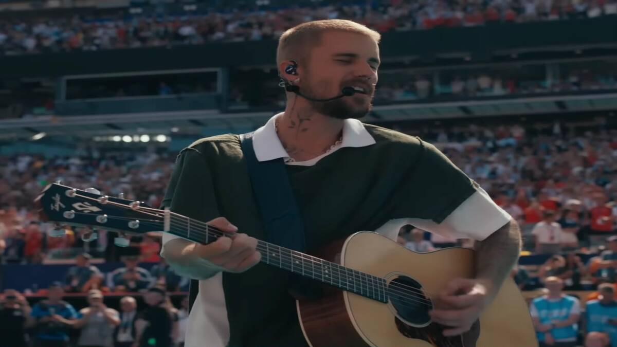 Justin Bieber canta e toca violão durante o show do intervalo da final da Copa do Mundo de 2026, realizado em um estádio lotado.