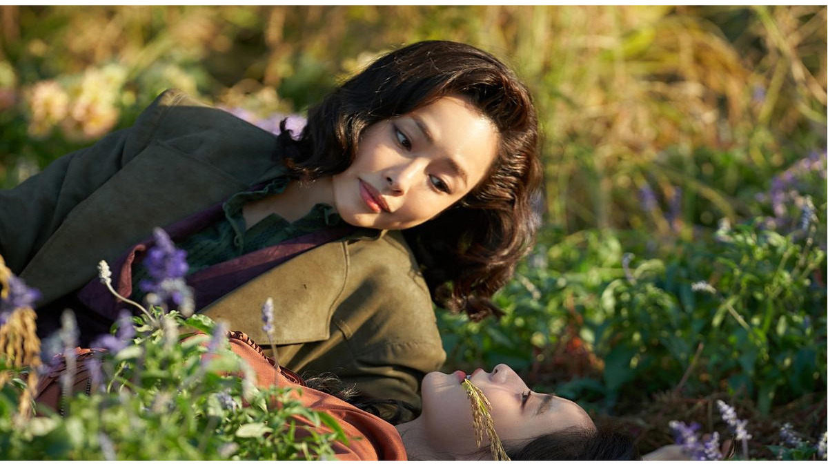 Duas mulheres deitadas em um campo florido em uma cena da série sul-coreana Madame Aema, ambientada na Coreia do Sul durante a década de 1980.