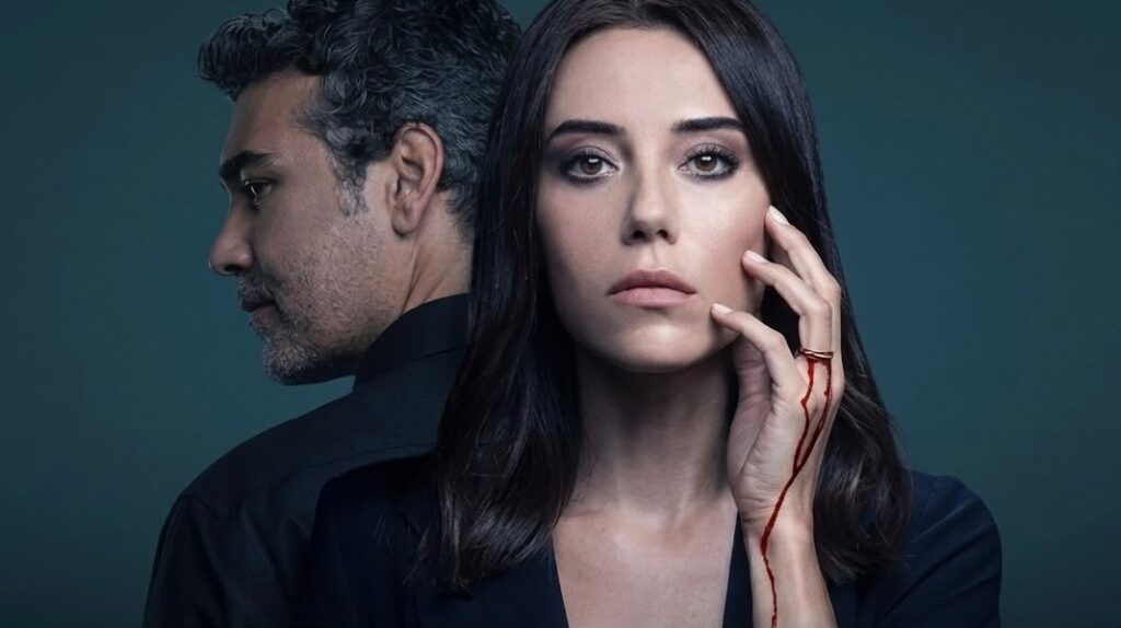 Pôster de divulgação da novela "Iludida" (Sadakatsiz), da Record TV, mostrando um casal em close. No primeiro plano, uma mulher olha seriamente para a frente com a mão no rosto, usando um anel de noivado de onde escorre sangue. Atrás dela, um homem de cabelos grisalhos está de costas, olhando para o lado. O título da novela aparece na parte inferior.