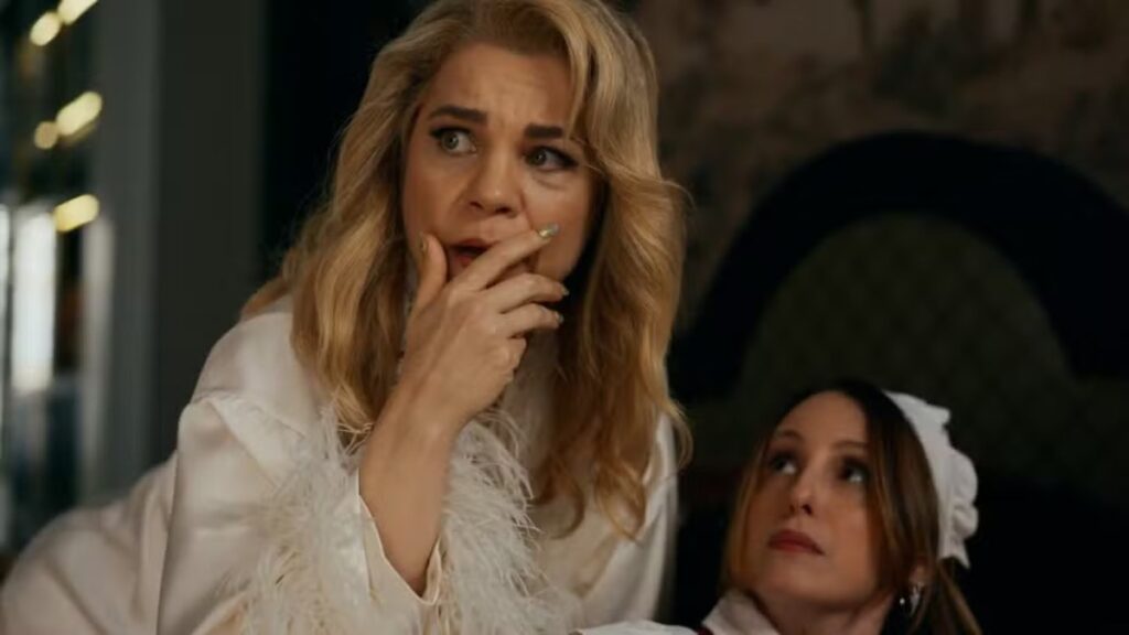 Pilar reage com expressão de choque ao descobrir um problema, enquanto outra mulher observa a situação em cena de novela.