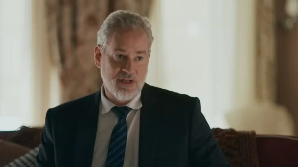 Homem grisalho de terno e gravata aparece sentado em um ambiente elegante na novela Quem Ama Cuida
